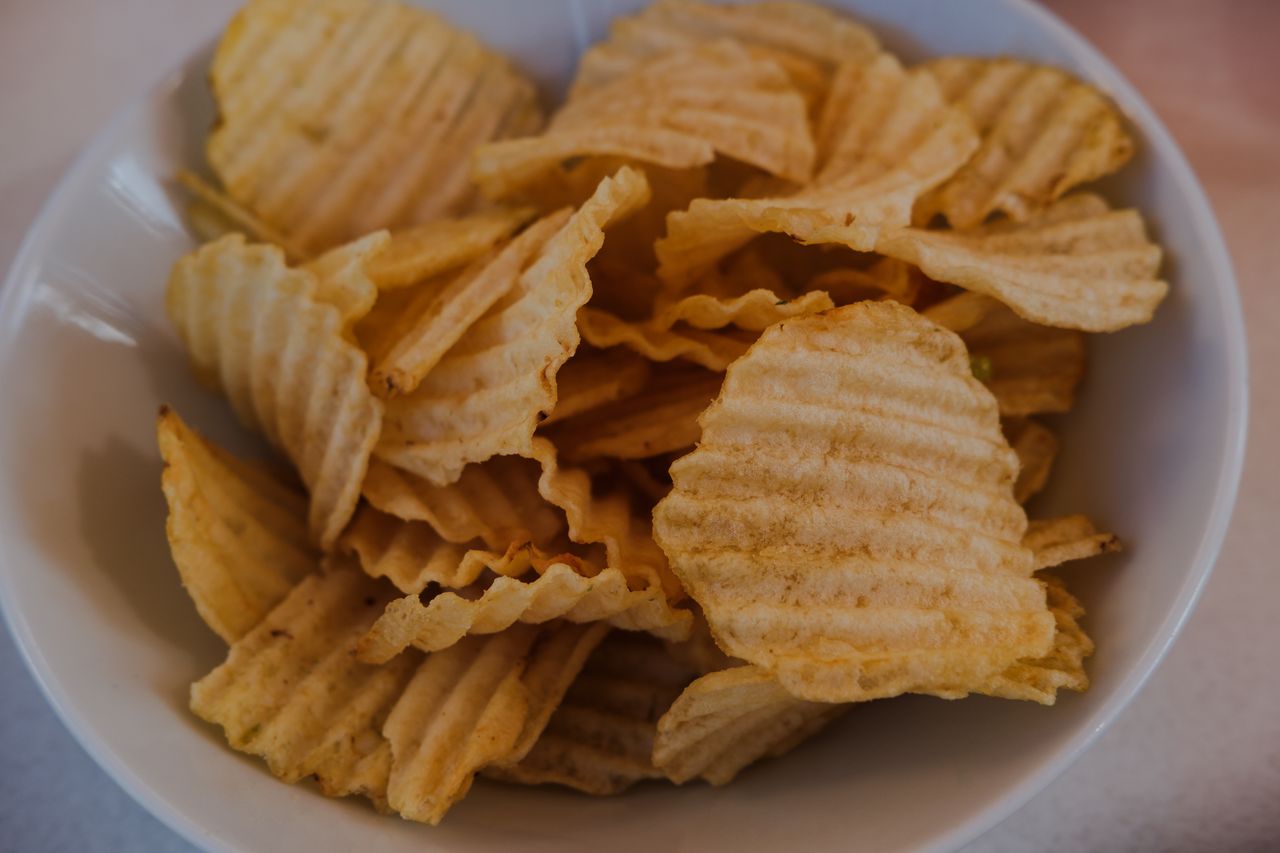 Delicious, golden ridged potato chips in a white bowl, perfect for snacking.